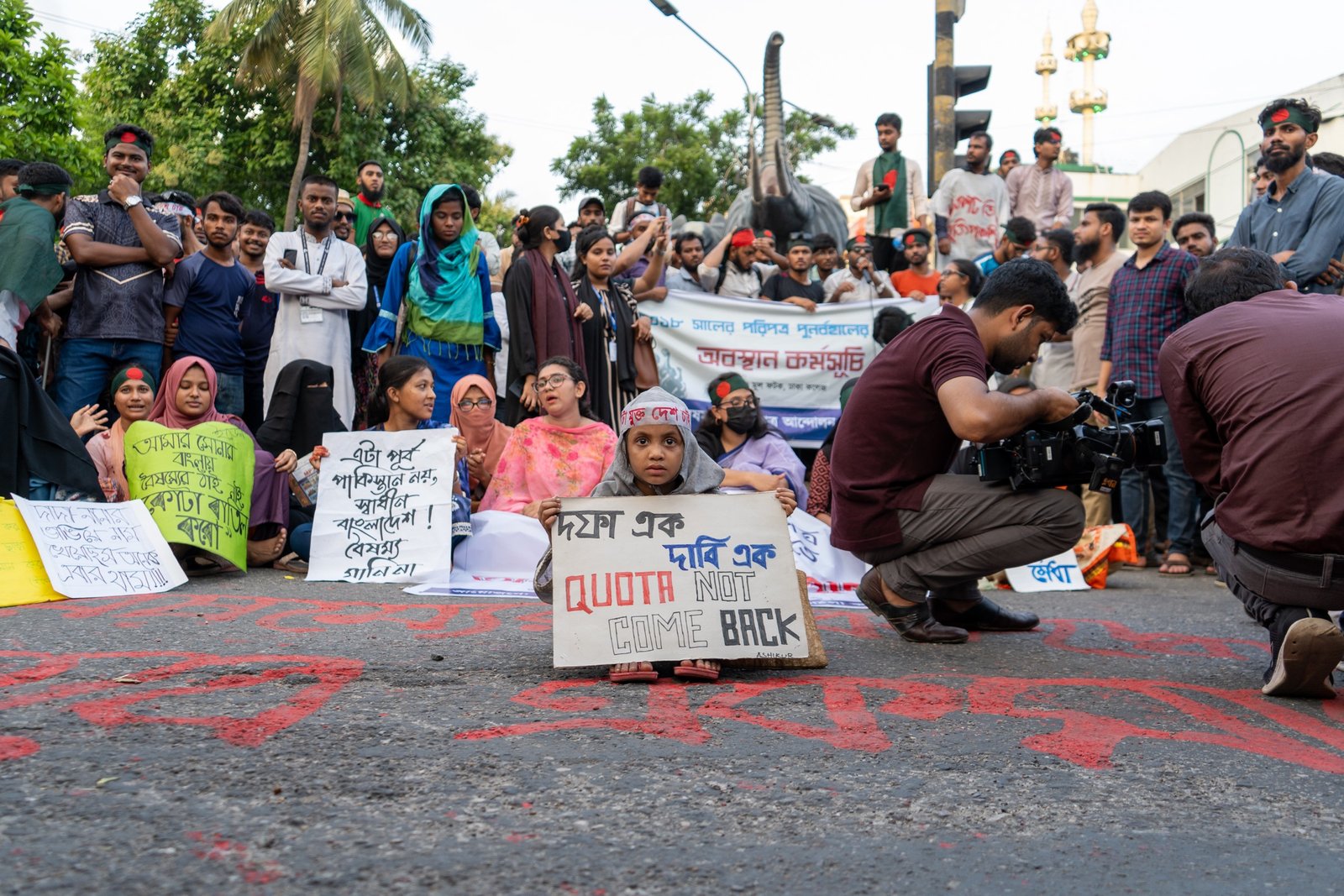 Protesters gathered in the street with handmade signs and camera crews nearby