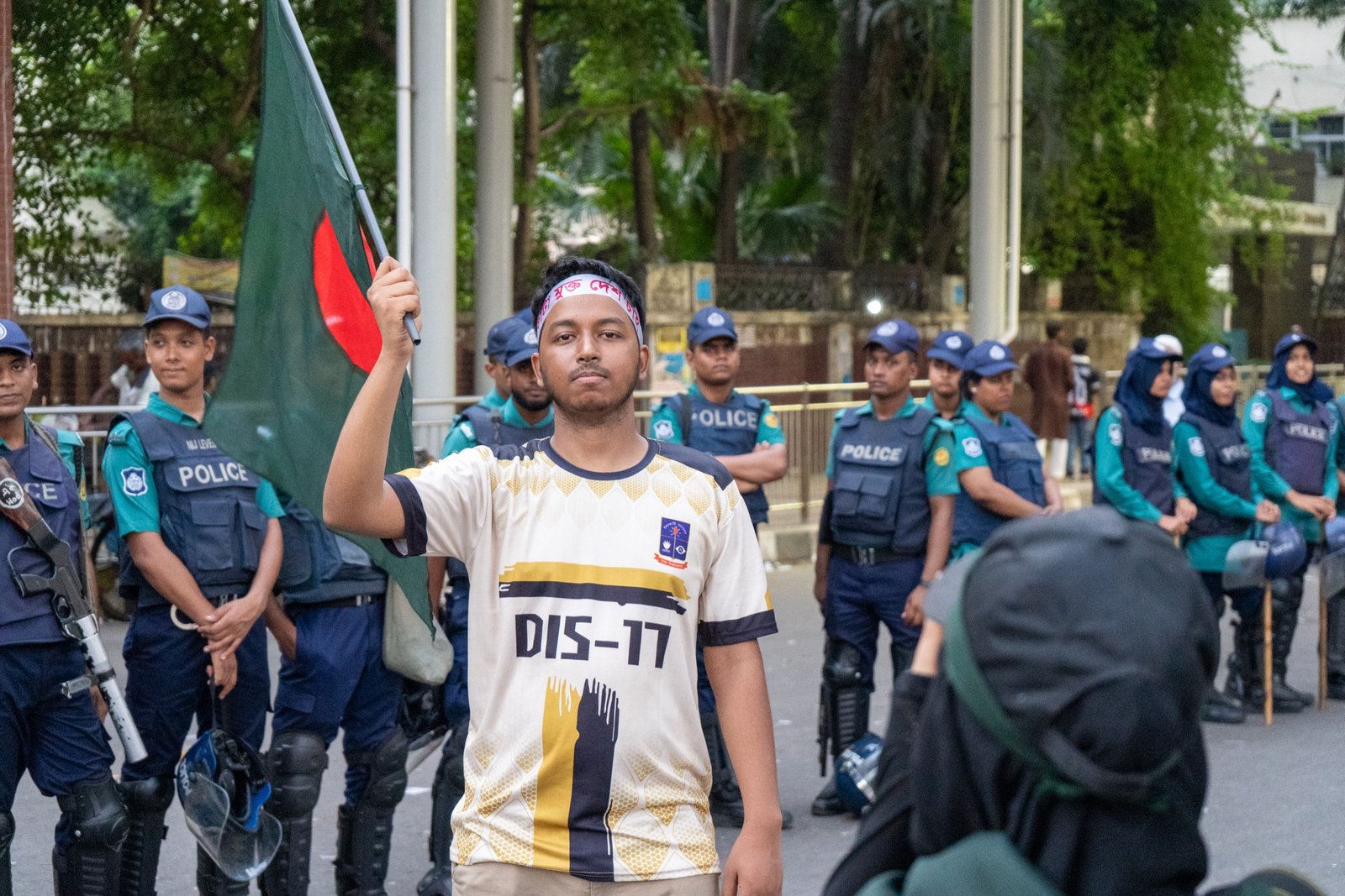Young protester raising a flag while police stand behind him