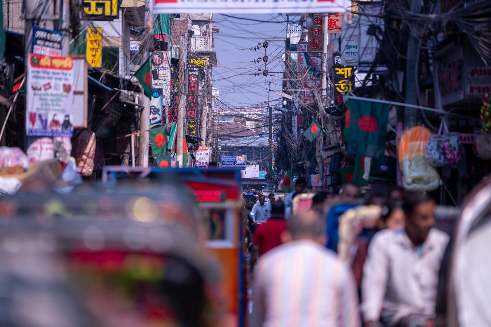 Dense urban street lined with Bangladesh flags and overhead wires