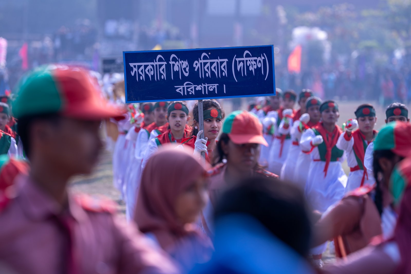 Schoolgirls in red and white uniforms marching in formation holding a banner during Victory Day parade