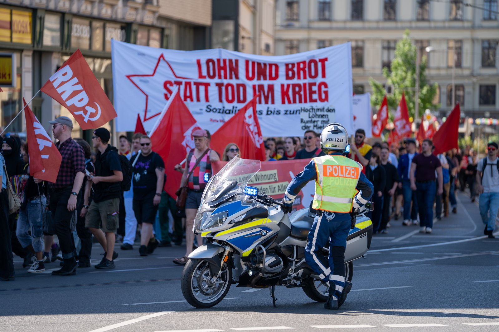 Red flags, an anti-war banner, and a police motorcycle during the Leipzig Labor Day march