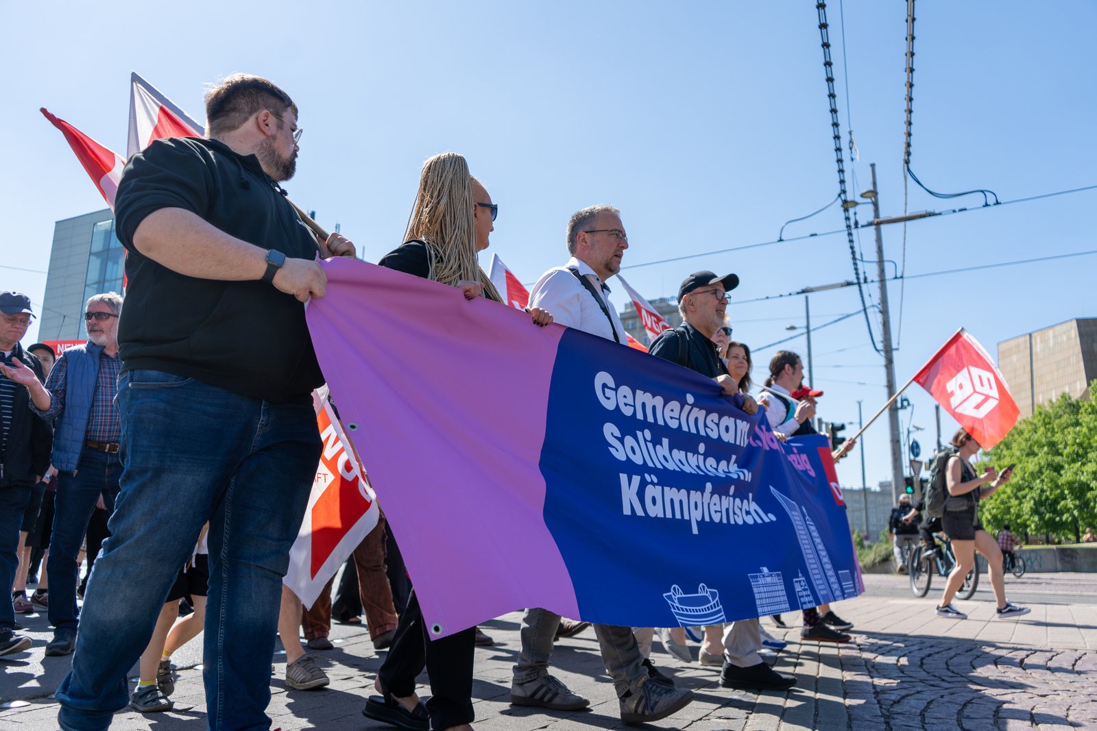Low-angle view of marchers carrying union banners and red flags through Leipzig