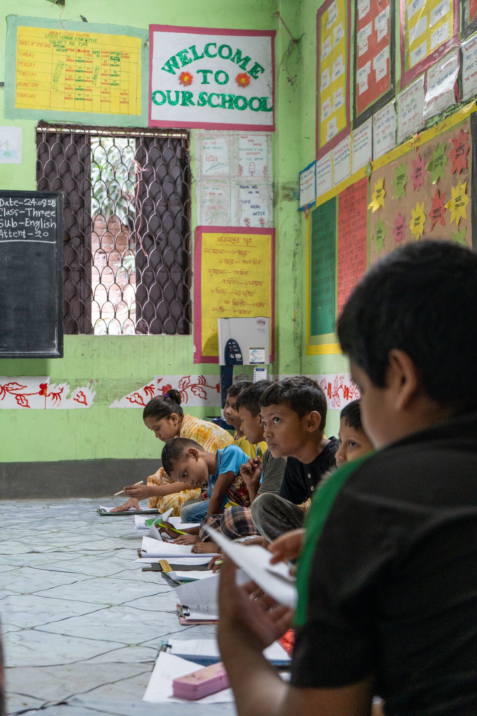 Children seated on the floor of a brightly painted classroom working on lessons