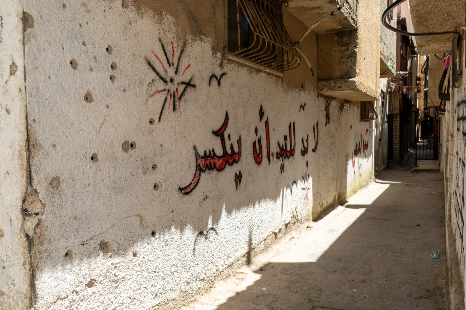Narrow alley in Nablus with bullet holes in the plaster walls and Arabic resistance graffiti