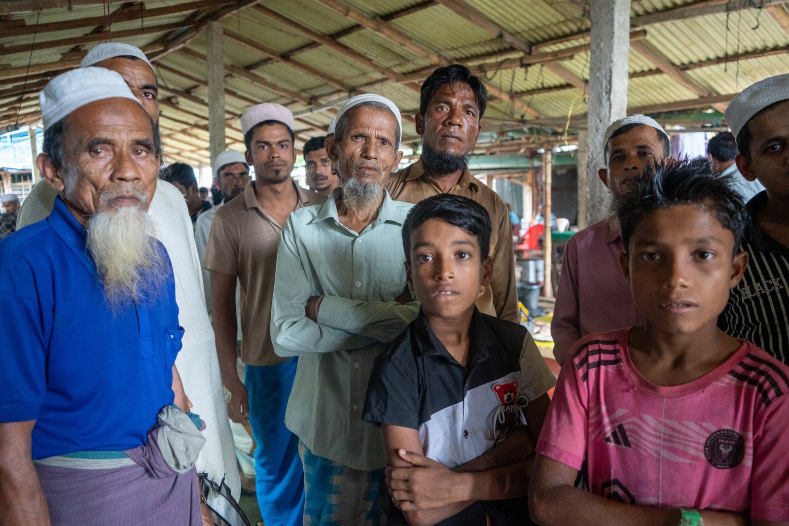 Rohingya men and boys gathered under a covered stall or market shelter