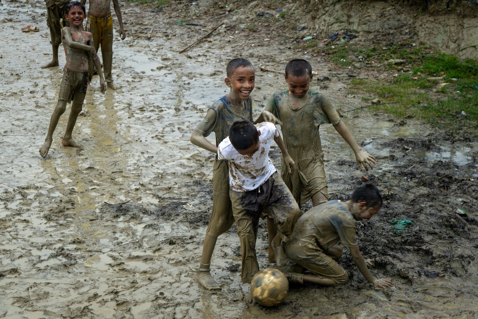 A mud-covered Rohingya child laughing after moving through flood-wet ground