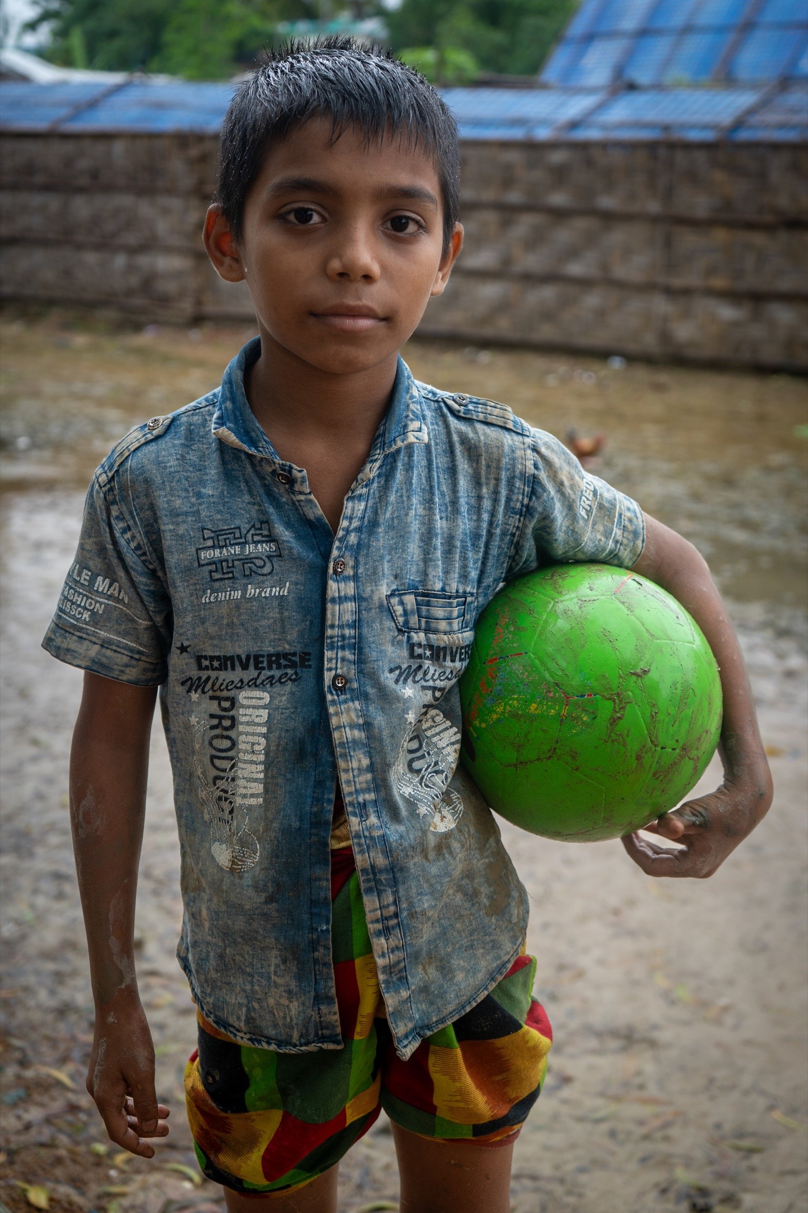 Close portrait of a Rohingya boy in denim holding a bright green ball