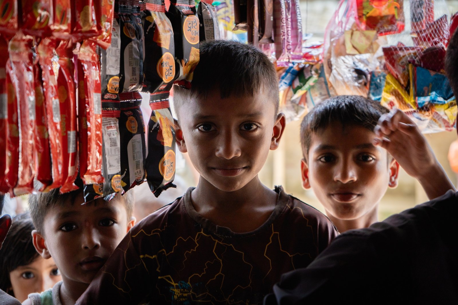 Rohingya boys standing at a snack stall with hanging packets and goods