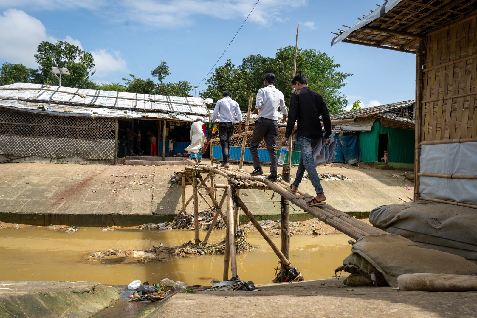Rohingya people crossing a bamboo bridge over an open sewage channel