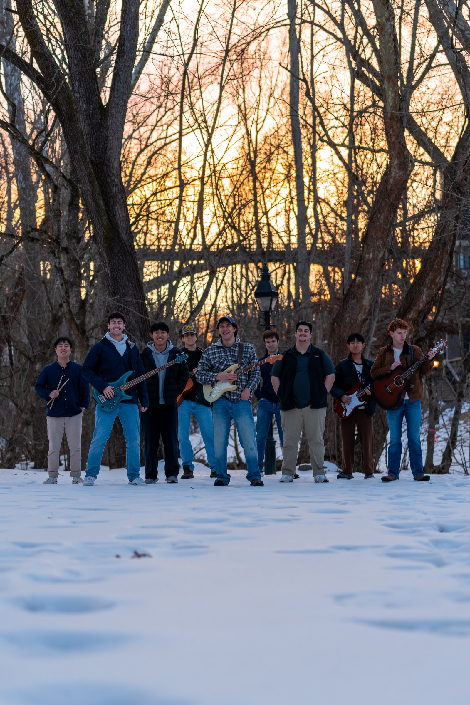 Band of young men standing in a line with their instruments in a snowy field against a warm sunset sky