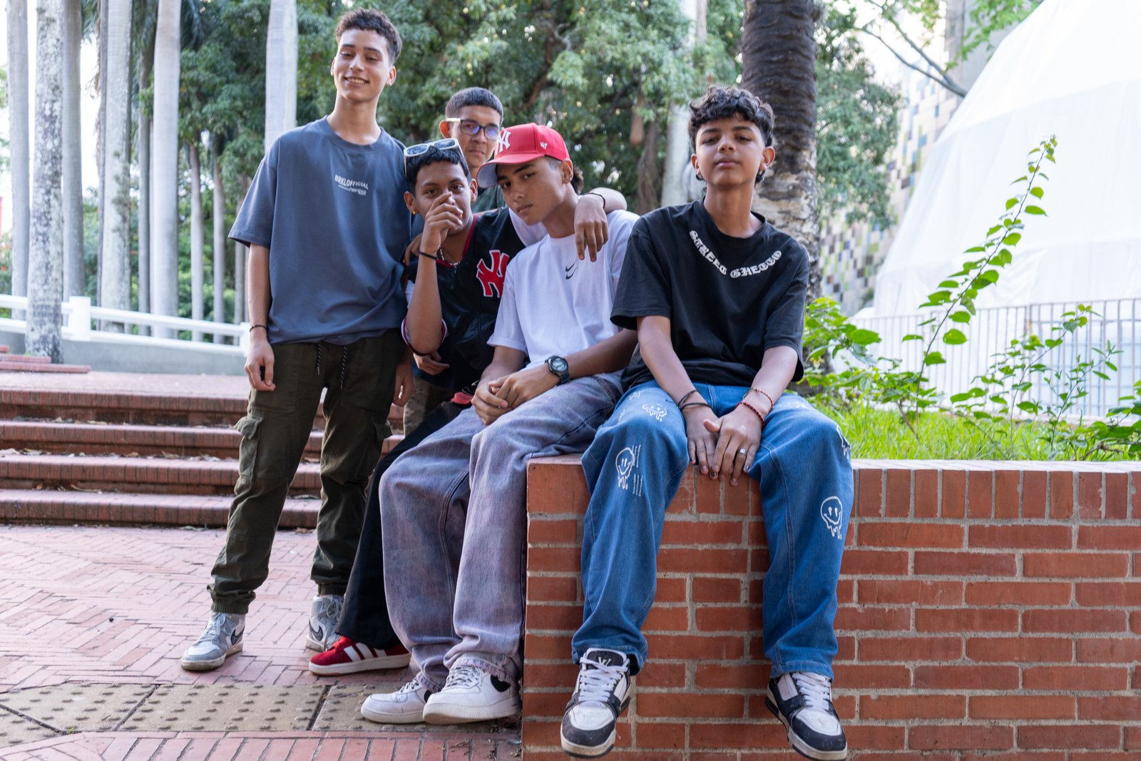 Five young men posing casually on outdoor brick steps with trees and buildings behind them