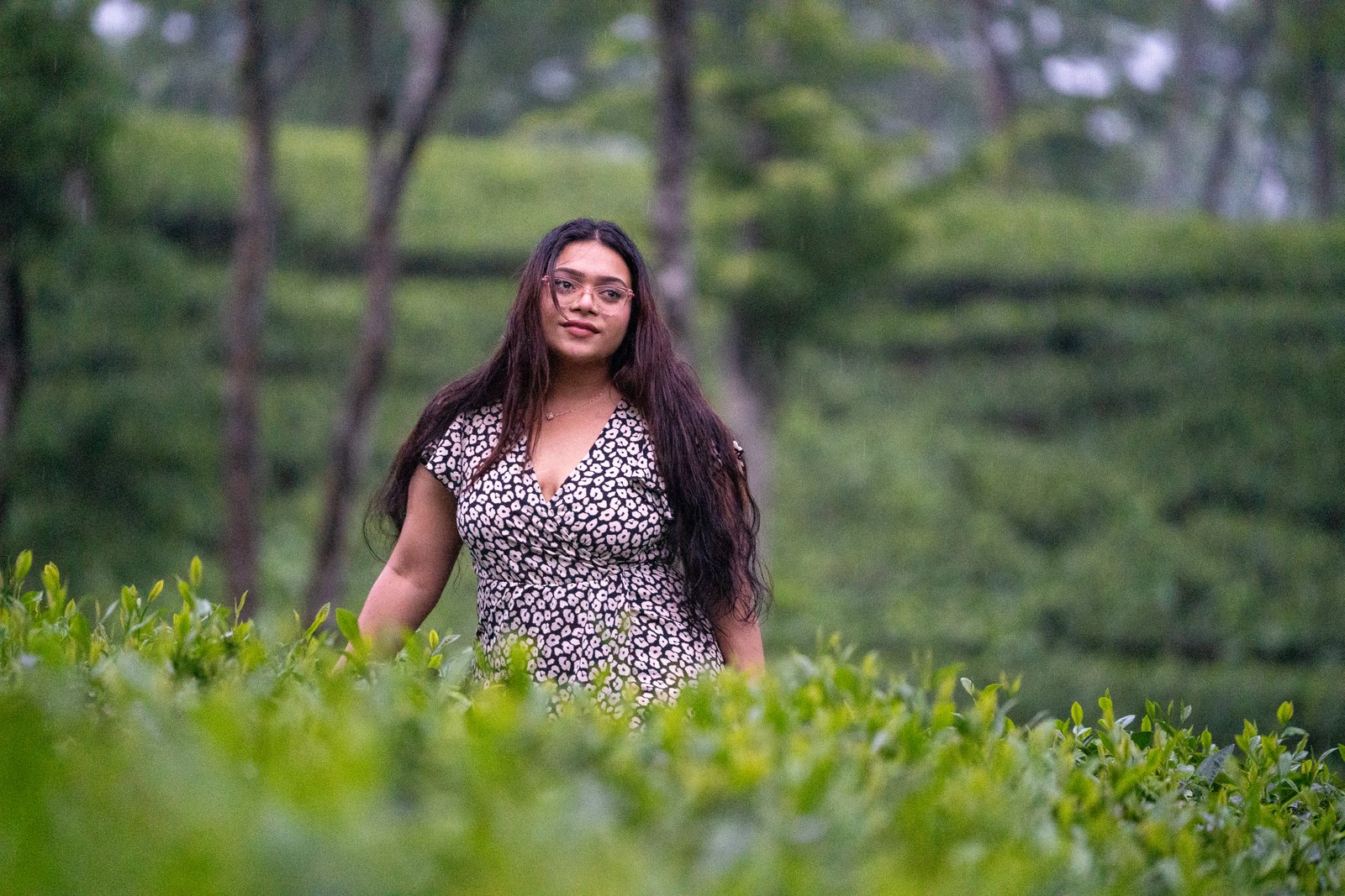 Woman in a floral dress standing among lush green tea plants in a misty plantation