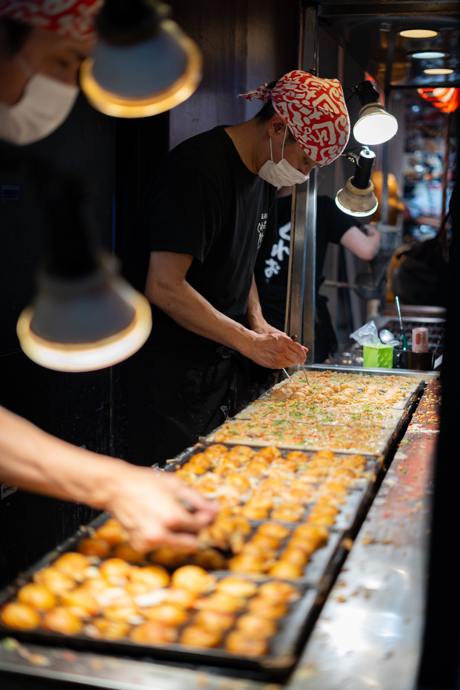 Cook preparing food at a night market griddle under warm task lights